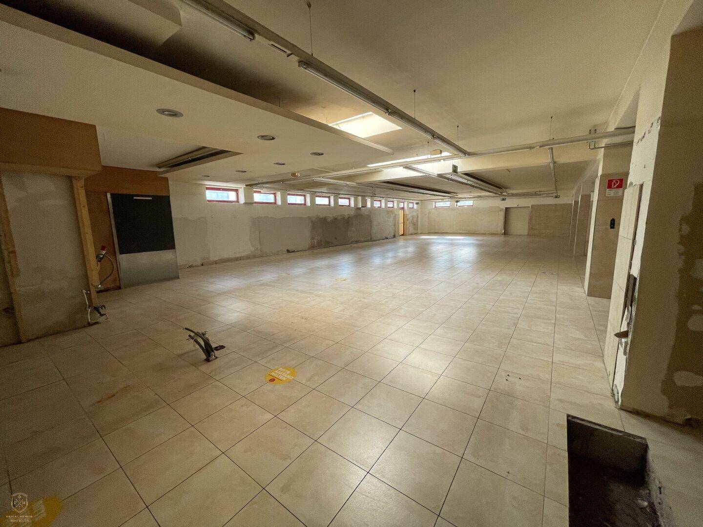 Geräumiger, leerstehender Gewerberaum mit Fliesenboden und vielen kleinen Fenstern entlang der Wand.