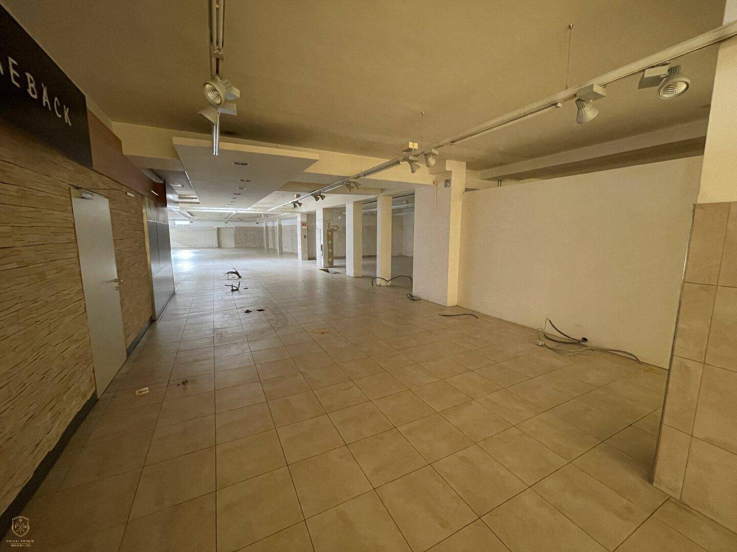 Weitläufiger, leerer Gewerberaum mit Fliesenboden, Säulen und Deckenbeleuchtung, bereit für den Ausbau.