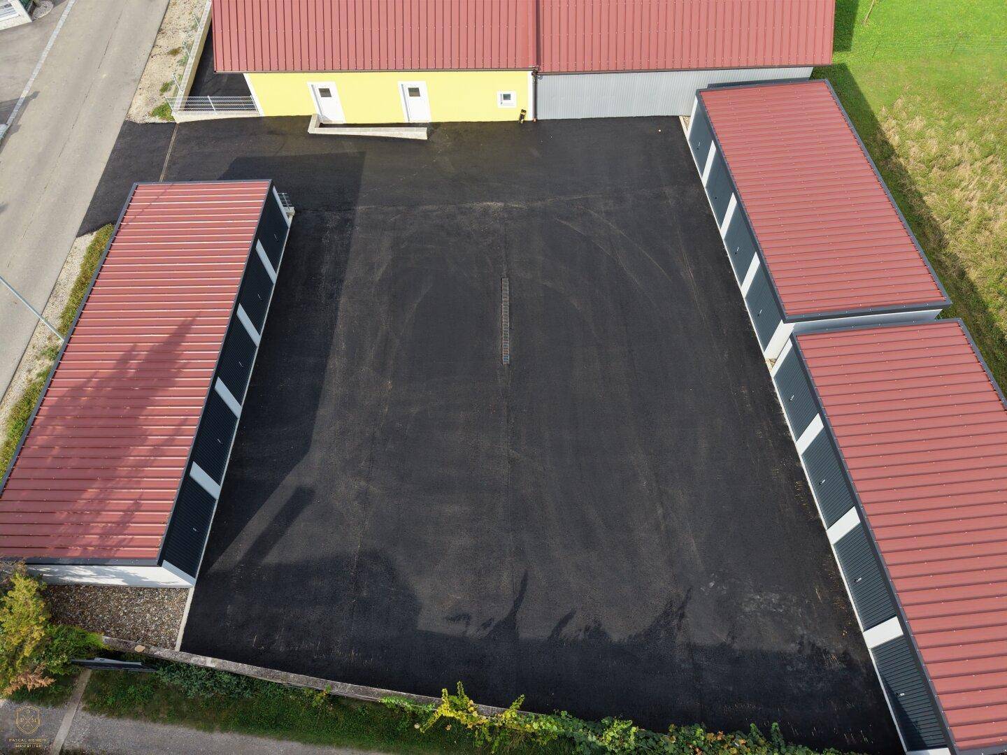 Luftaufnahme des gesamten Anwesens mit mehreren Garagenkomplexen, einem Wohnhaus und weitläufigen asphaltierten Bereichen.