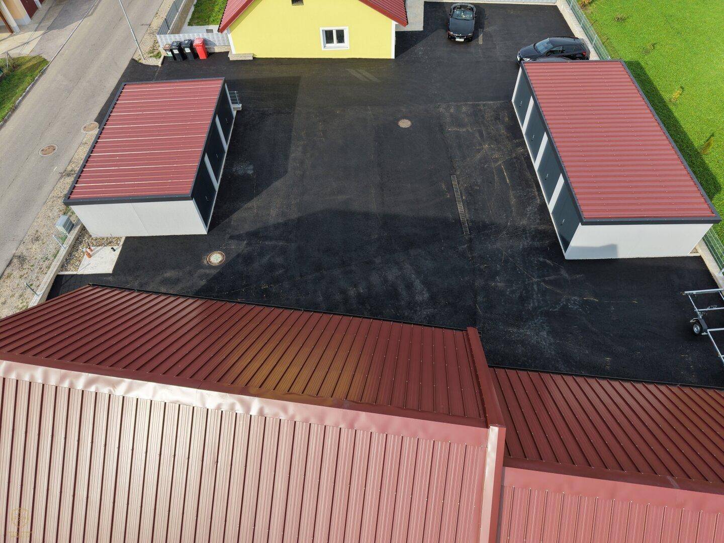 Luftaufnahme des Anwesens mit mehreren Garagengebäuden, einem gelben Haus und großzügigen asphaltierten Flächen.