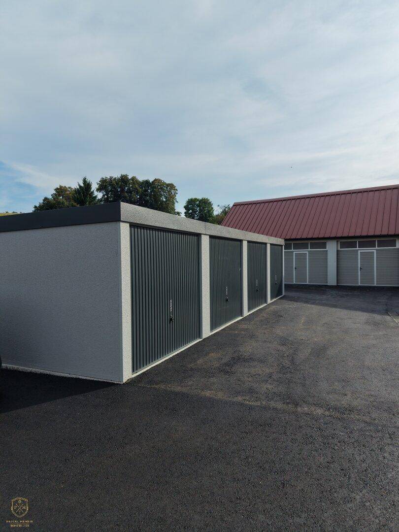 Ansicht einer modernen Garagenreihe mit dunklen Toren und heller Fassade, angrenzend an eine asphaltierte Fläche.