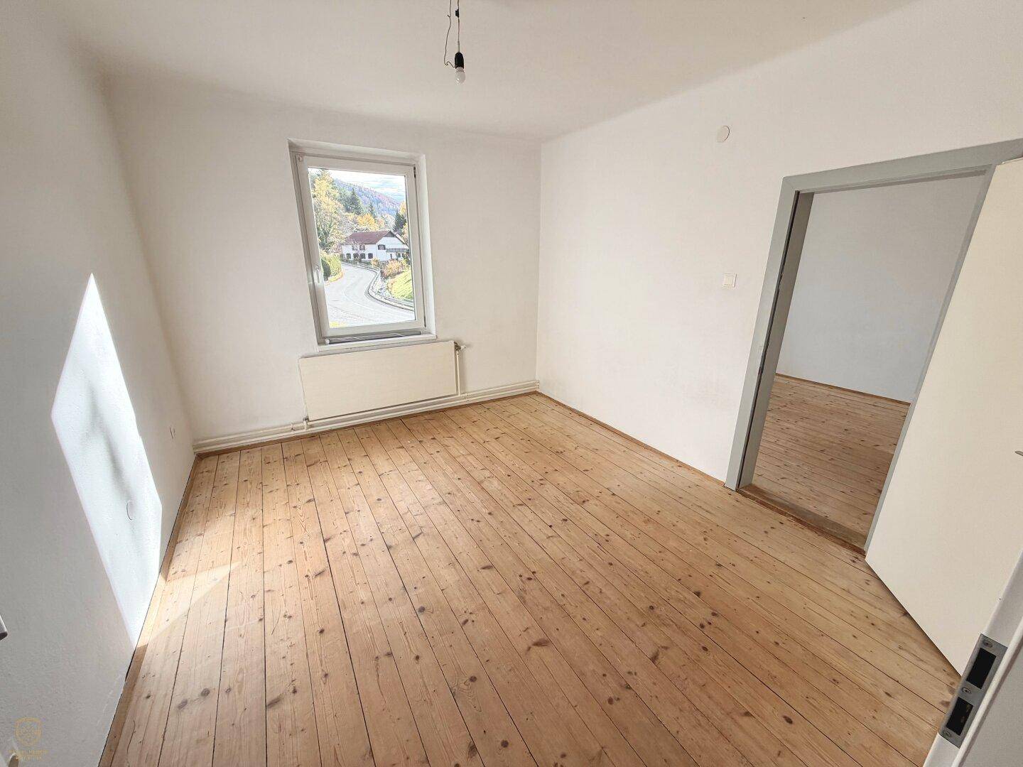 Helles Zimmer mit rustikalem Holzboden und Blick auf die umliegende grüne Landschaft.
