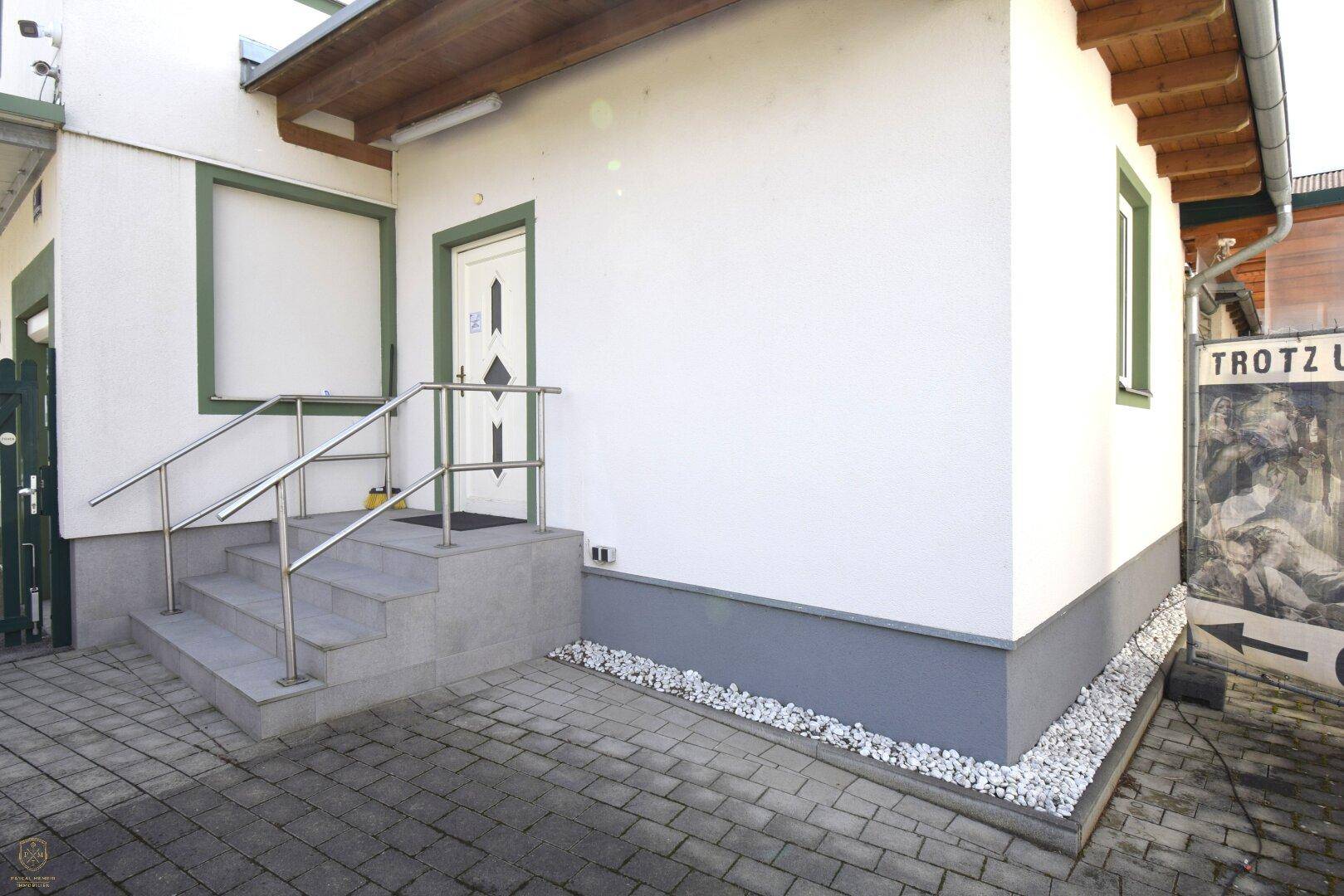 Eingangsbereich des Gebäudes mit Außentreppe, Geländer und gepflastertem Vorplatz.