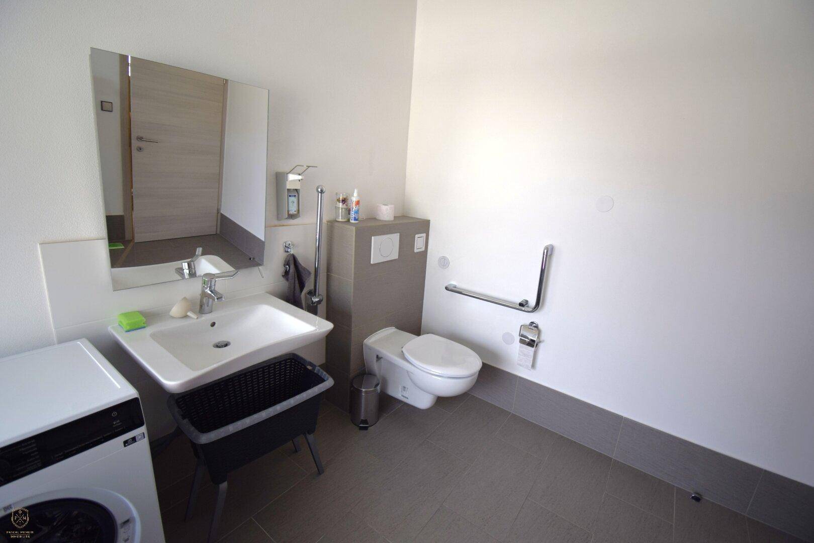 Barrierefreies Badezimmer mit Waschmaschine, WC und Haltegriffen für mehr Sicherheit.