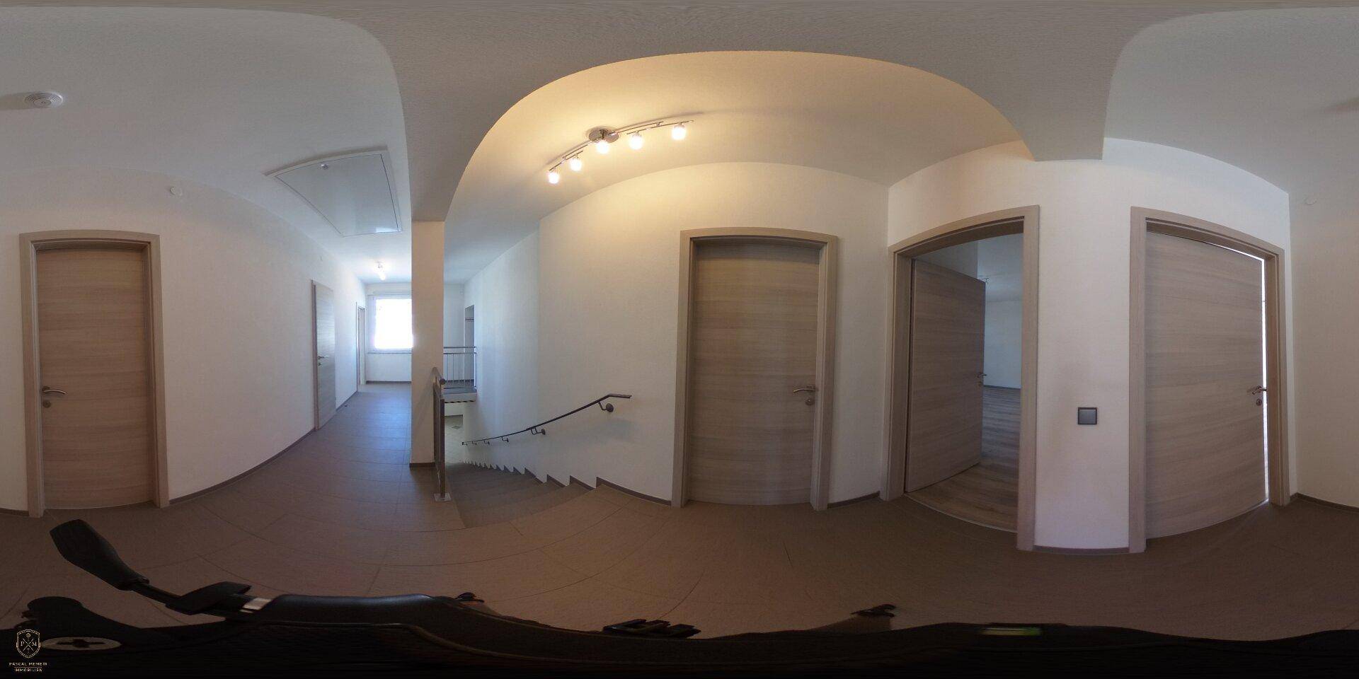Panoramaaufnahme eines hellen Flurs mit Treppenaufgang und mehreren Türen zu den Zimmern.