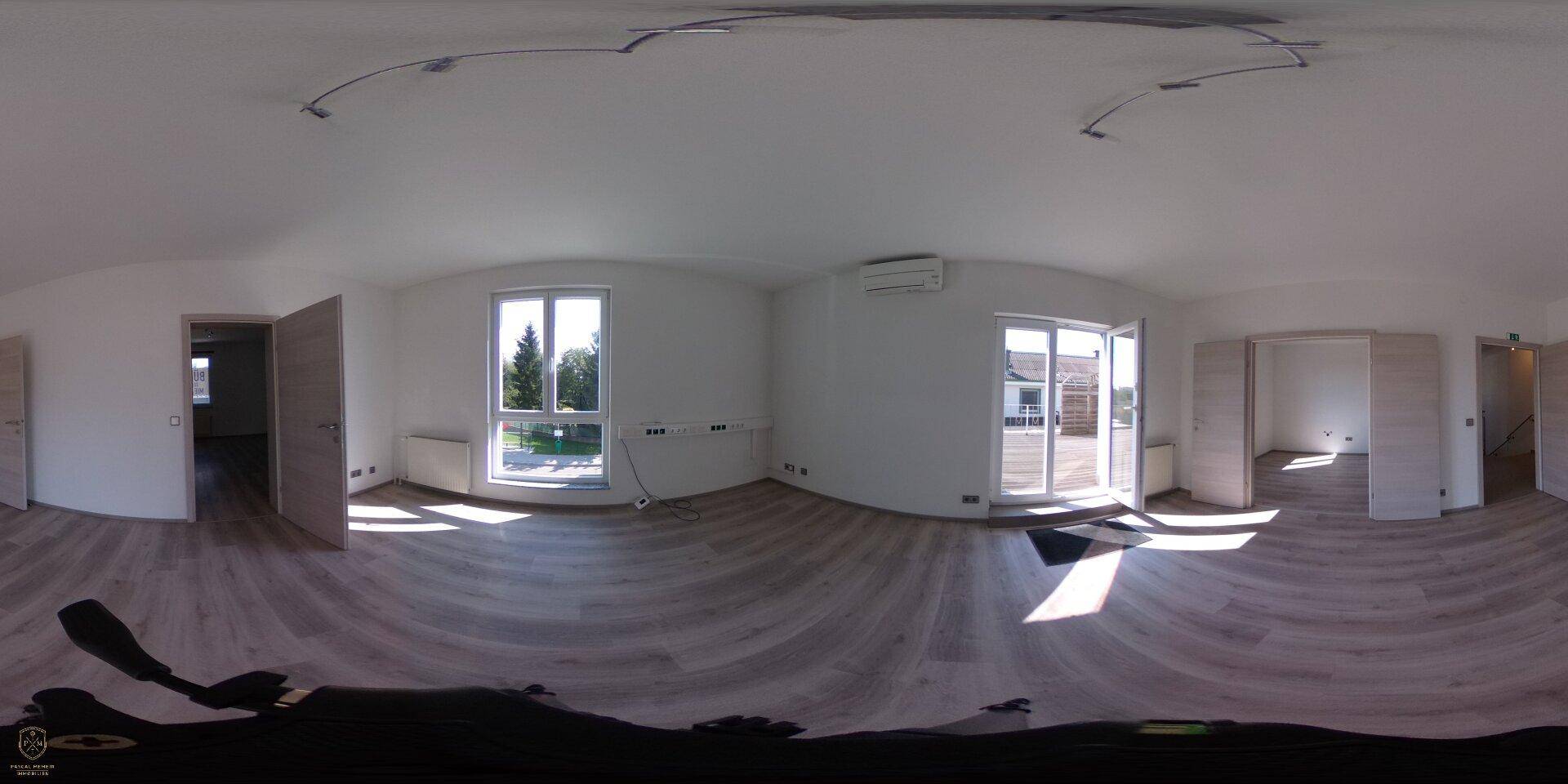 Panoramaaufnahme eines hellen Wohnzimmers mit Laminatboden, Klimaanlage und Terrassenzugang.