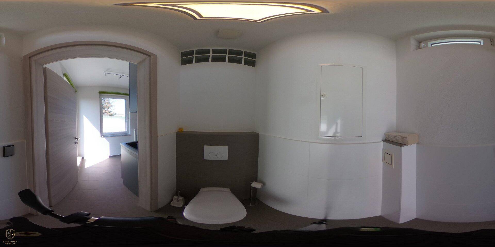 Helles Badezimmer mit wandhängender Toilette, einem Fenster und schlichten, weißen Wänden.