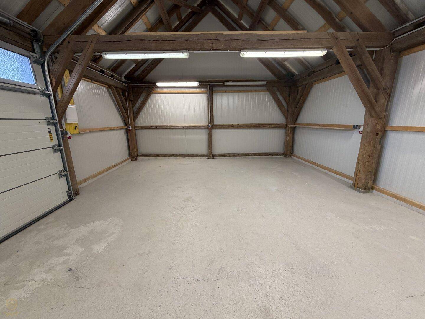 Helle und geräumige Garage mit Holzbalken und robustem Betonboden.