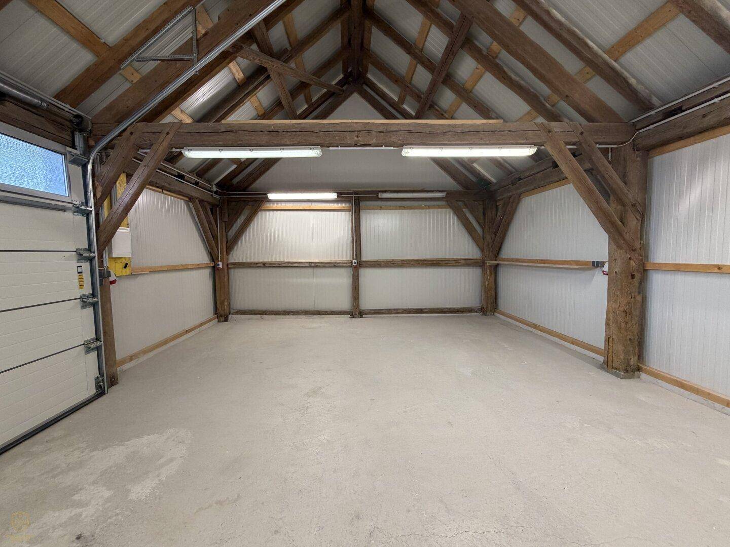 Geräumige Garage mit hohen Decken, sichtbaren Holzbalken und Betonboden.