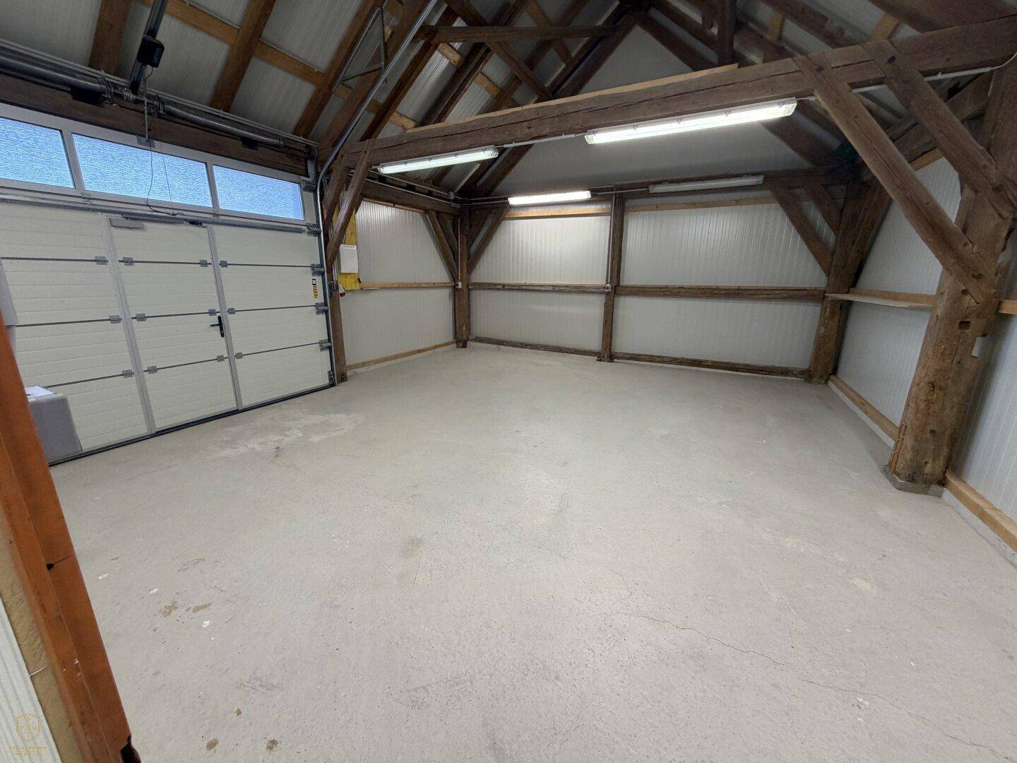 Geräumige Garage mit großem Tor, sichtbaren Holzträgern und Betonboden.