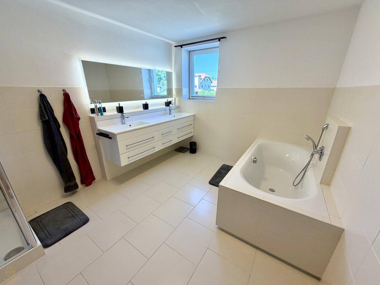 Modernes Badezimmer mit Doppelwaschbecken, Badewanne und großem beleuchtetem Spiegel.