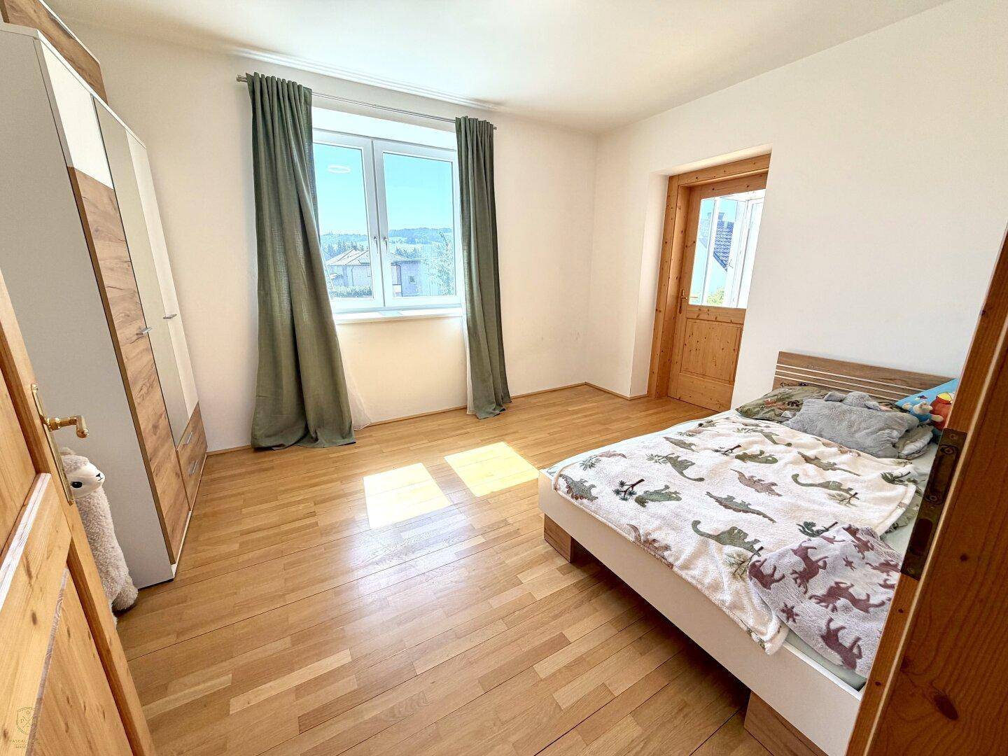 Helles Schlafzimmer mit Holzboden, großem Fenster und modernem Kleiderschrank.