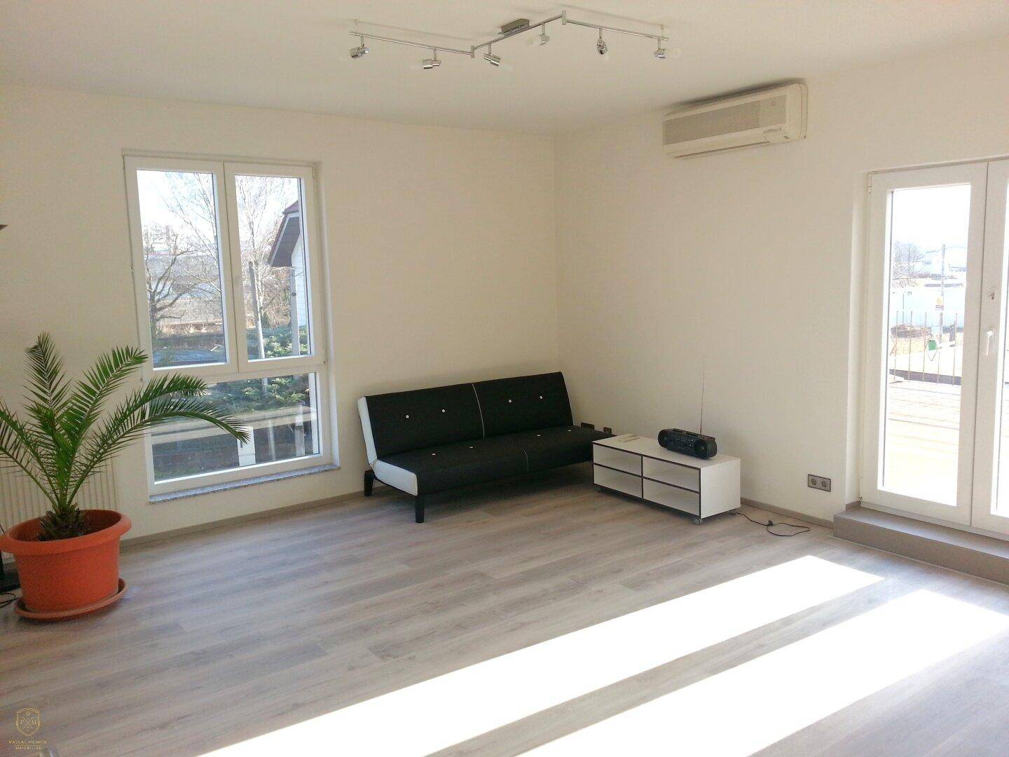 Heller Wohnraum mit Laminatboden, Klimaanlage und Zugang zu einem Balkon oder einer Terrasse.