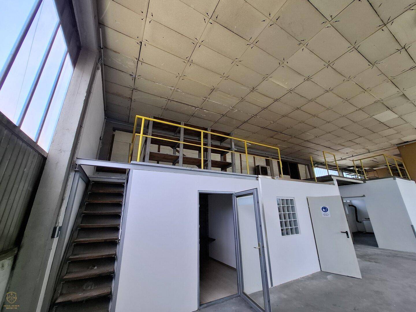 Große Industriehalle mit hohen Decken, Betonboden und einer Metalltreppe, die zu einer Empore führt.