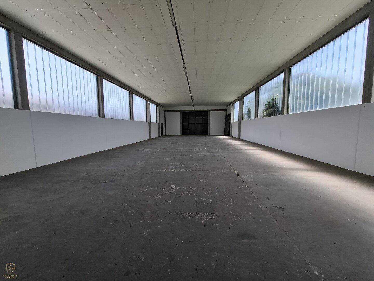Langer, leerer Lagerraum mit hohen Decken und durchgehenden Fensterbändern für viel Tageslicht.