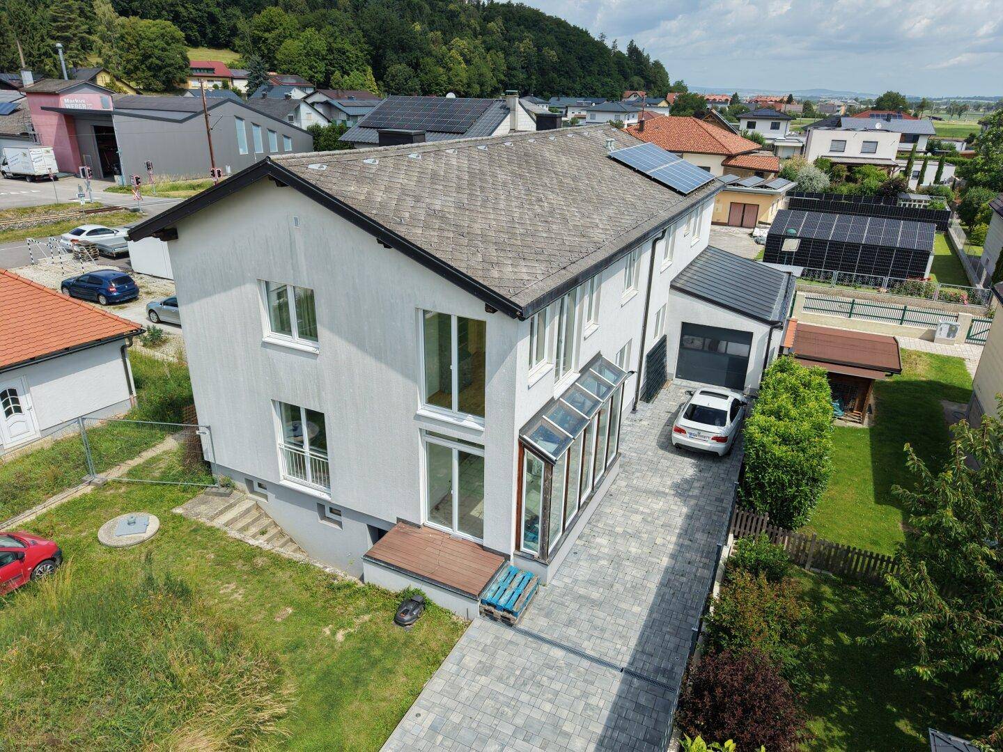 Luftaufnahme eines modernen Einfamilienhauses mit Wintergarten, gepflasterter Auffahrt und Solaranlage auf dem Dach.