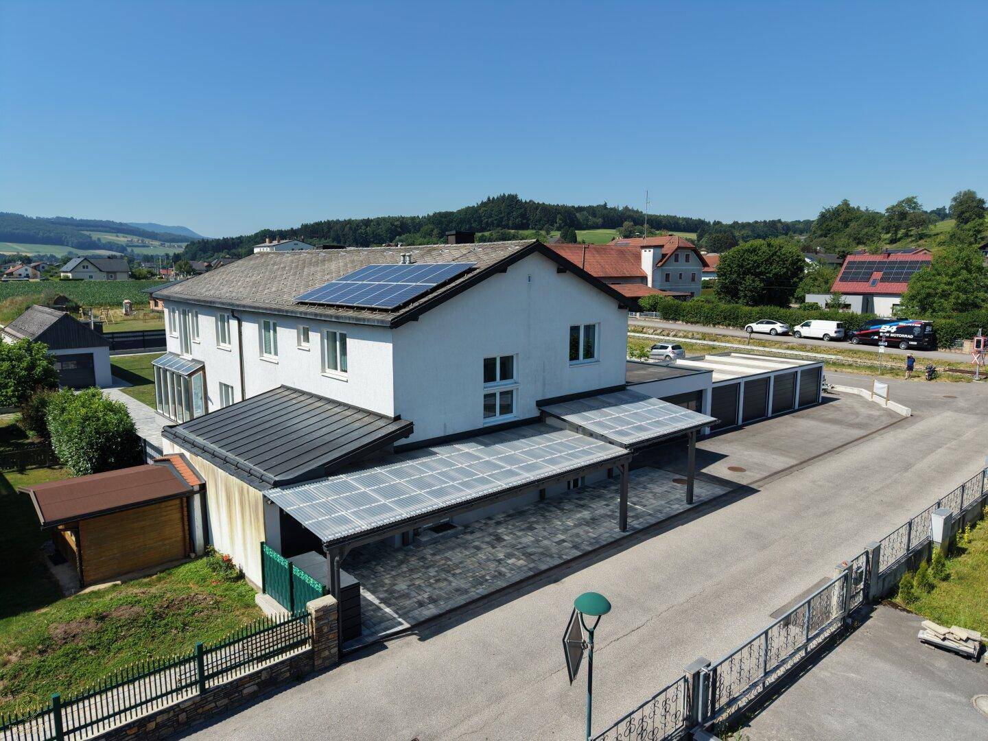 Weitläufige Ansicht des Hauses mit mehreren Carports, Solaranlagen auf dem Dach und ländlicher Umgebung.
