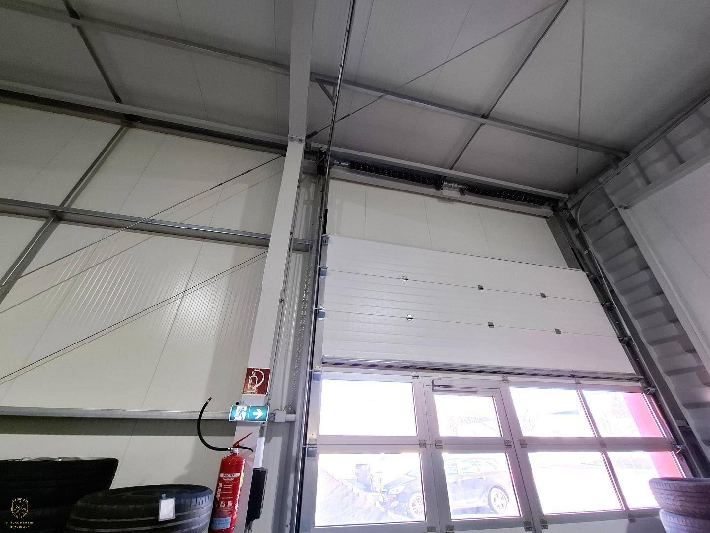 Blick auf ein großes Sektionaltor mit Fenstern und einen Feuerlöscher in einer Industriehalle.