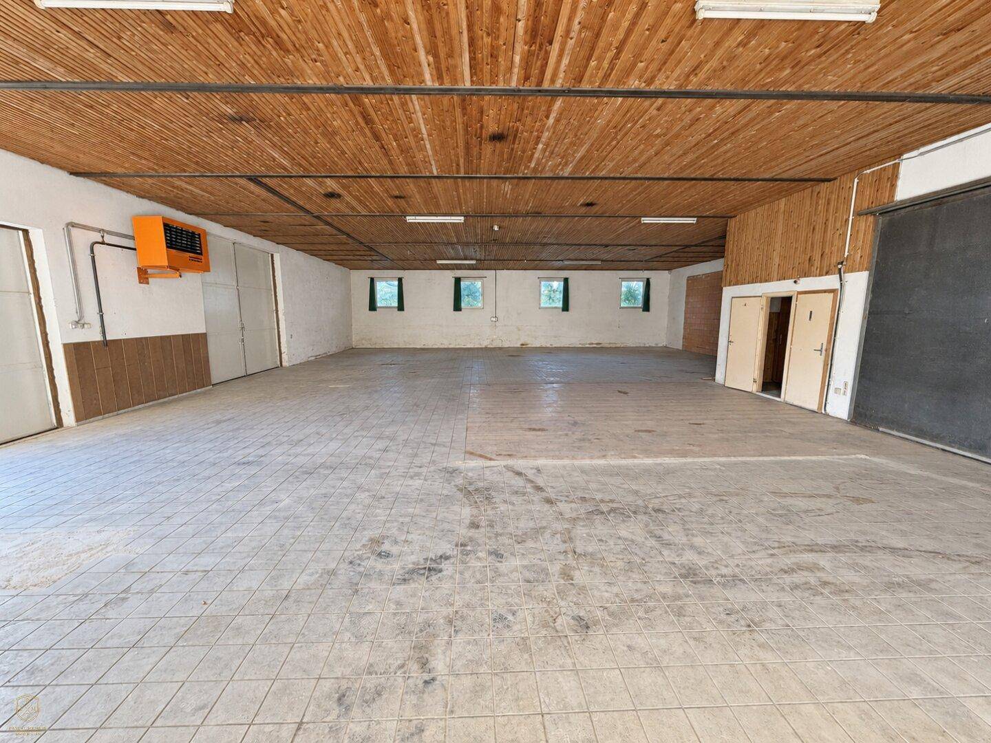 Weitläufiger Gewerberaum mit sichtbarer Holzdecke, Fliesenboden und mehreren Fenstern für Tageslicht.