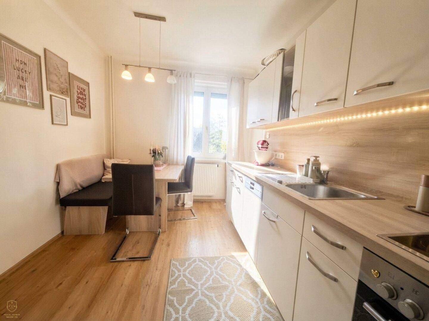 Helle Einbauküche mit Holzboden, integriertem Essbereich und Fenster mit Tageslicht.