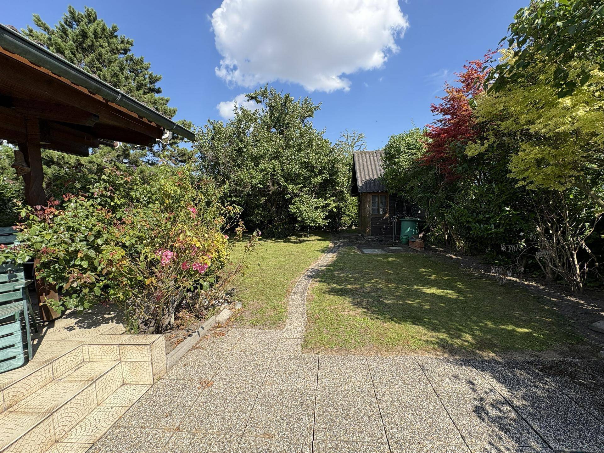 Idyllischer Gartenweg führt durch üppiges Grün zu einem weiteren kleinen Gebäude im Hintergrund.