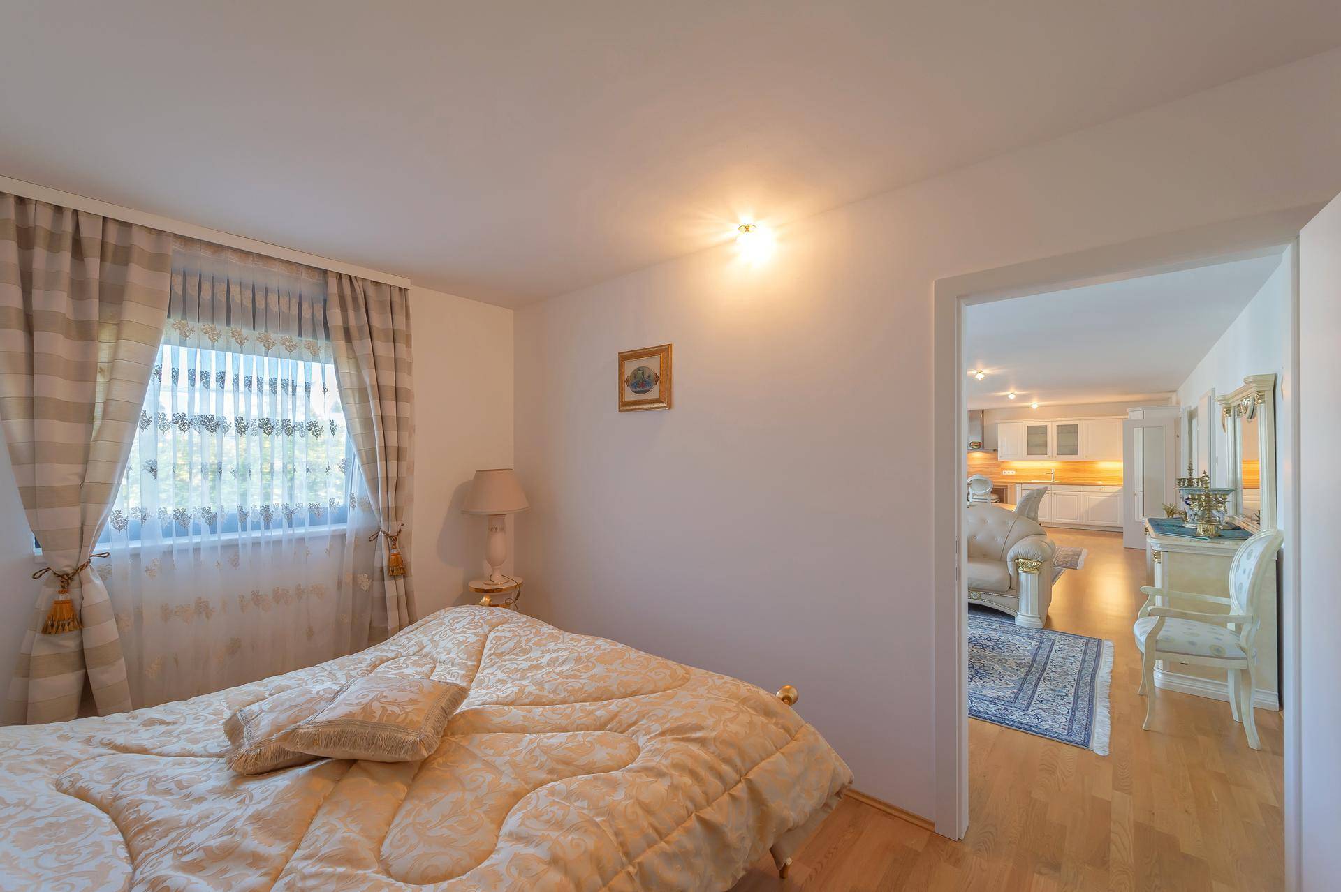 Schlafzimmer mit Doppelbett, Fenster und Blick in den angrenzenden Wohnbereich.