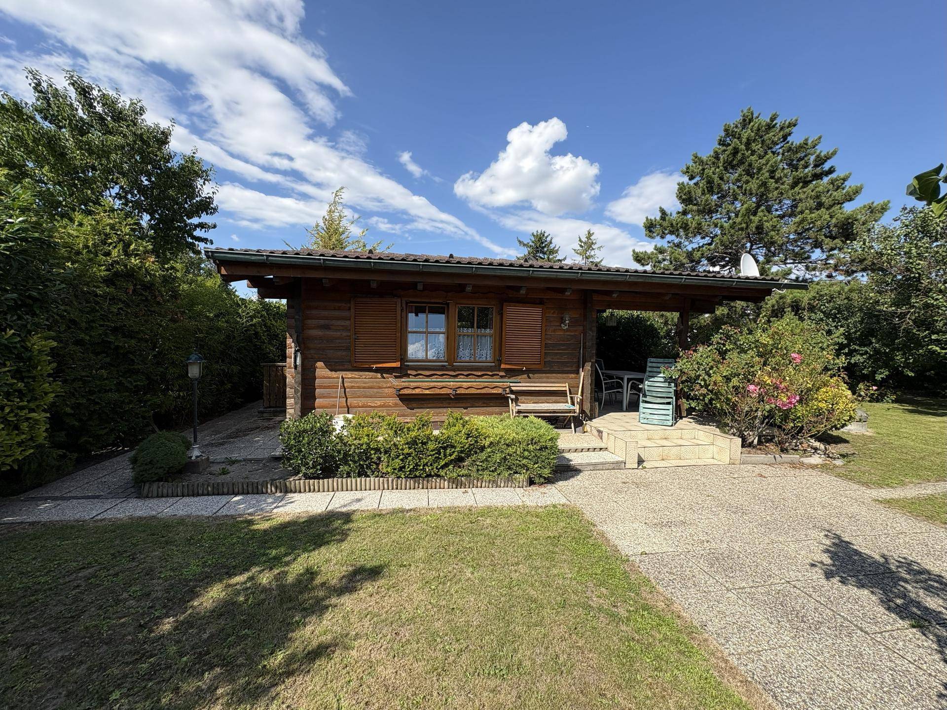 Charmantes Holzhaus umgeben von einem grünen Garten mit sonnigem Sitzbereich im Freien.
