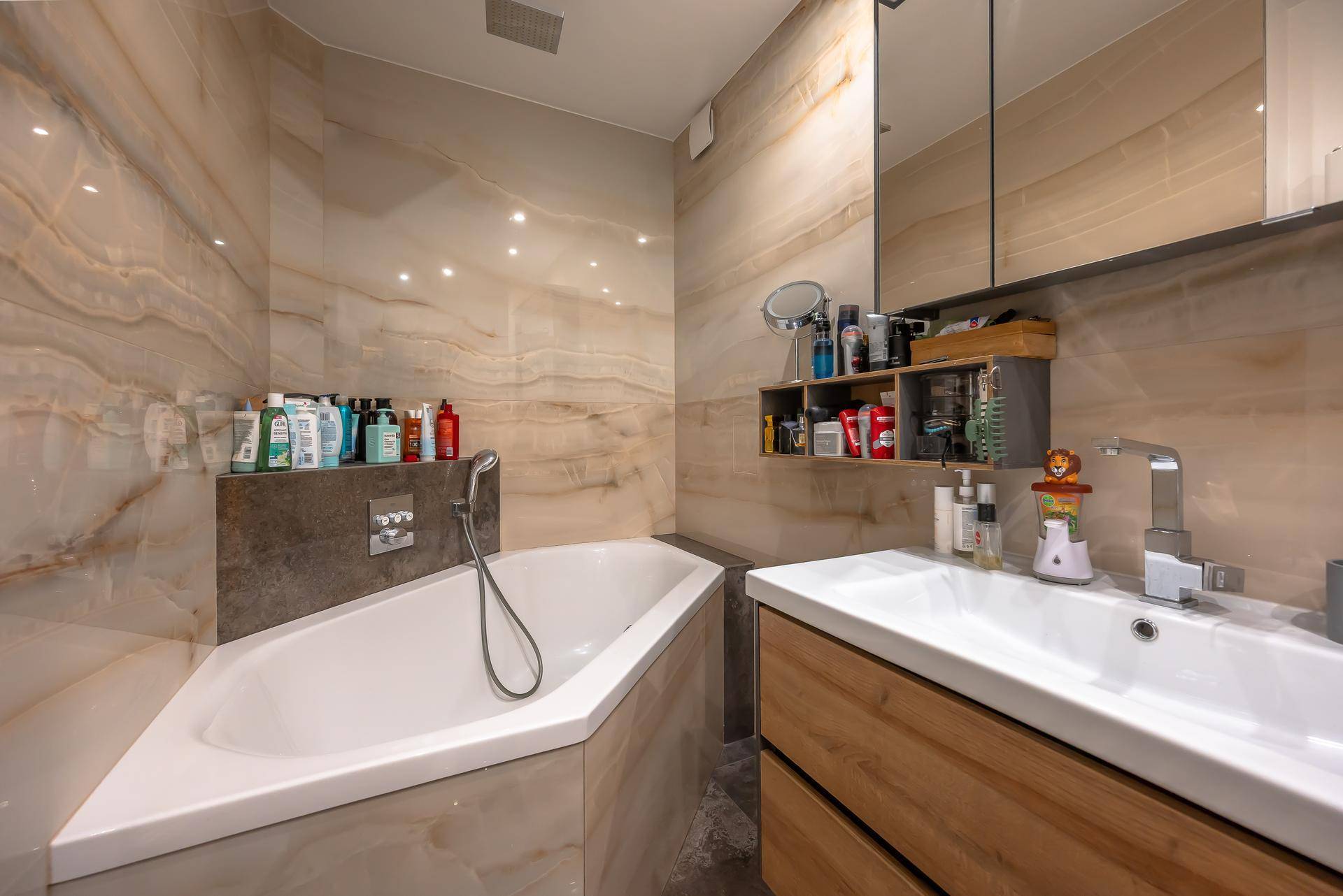 Modernes Badezimmer mit Eckbadewanne, Einzelwaschbecken und eleganten Marmorfliesen.