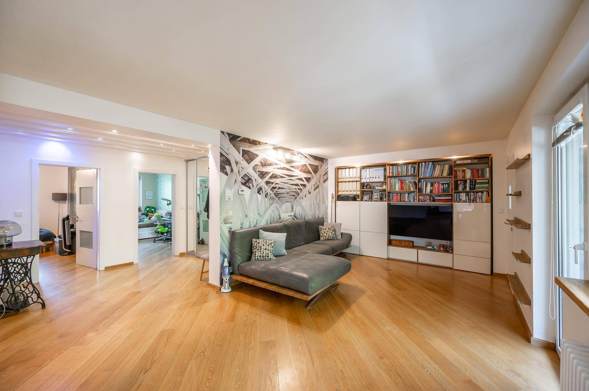 Geräumiges Wohnzimmer mit Holzboden, großem Sofa und integriertem Bücherregal.
