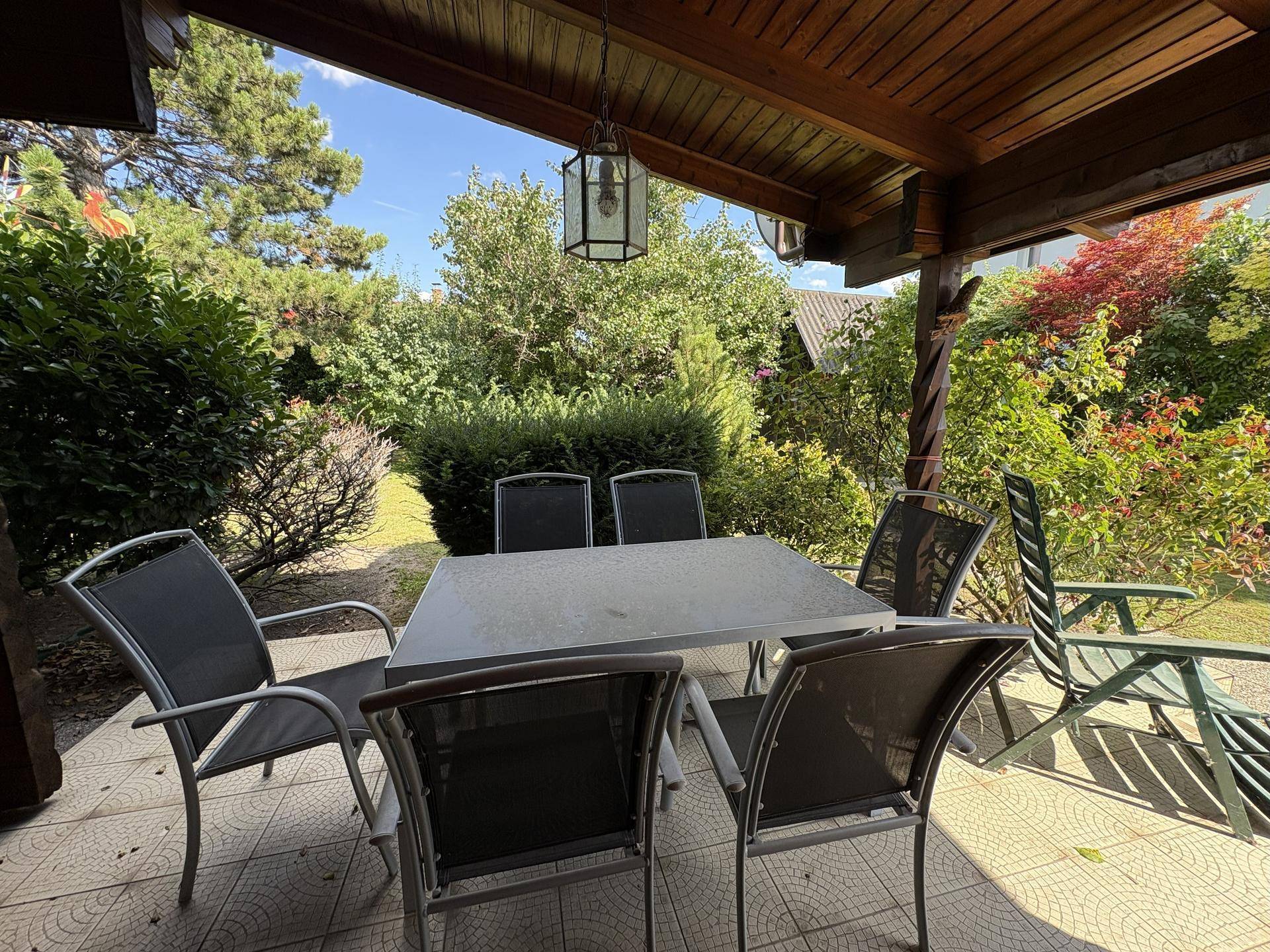 Gemütlicher Essbereich auf der überdachten Terrasse, umgeben von üppigem Grün und Bäumen.