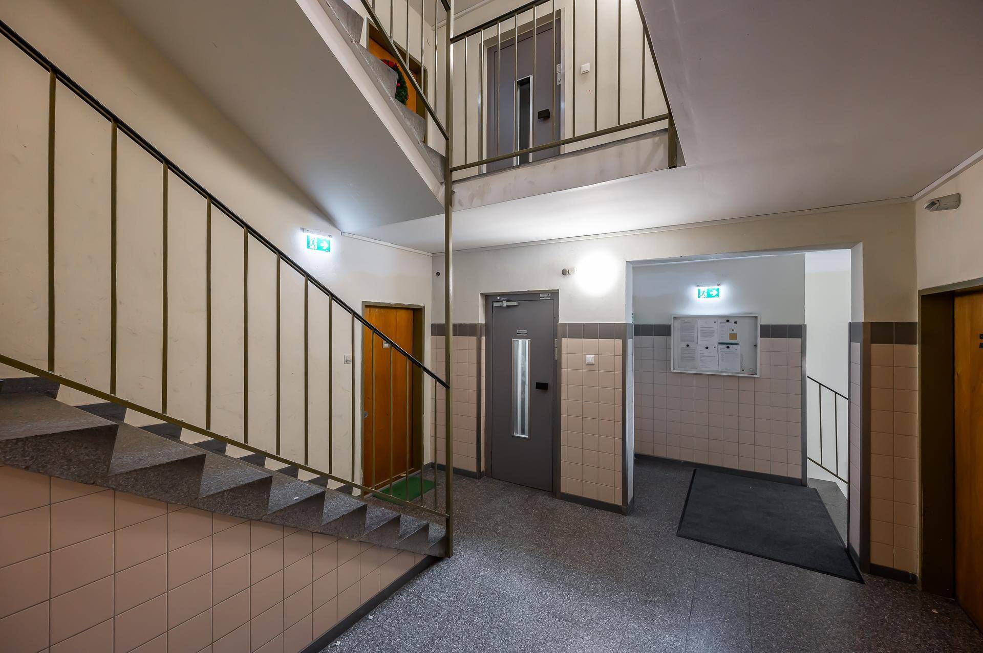 Treppenhaus eines Mehrfamilienhauses mit gefliestem Boden und Metallgeländer.
