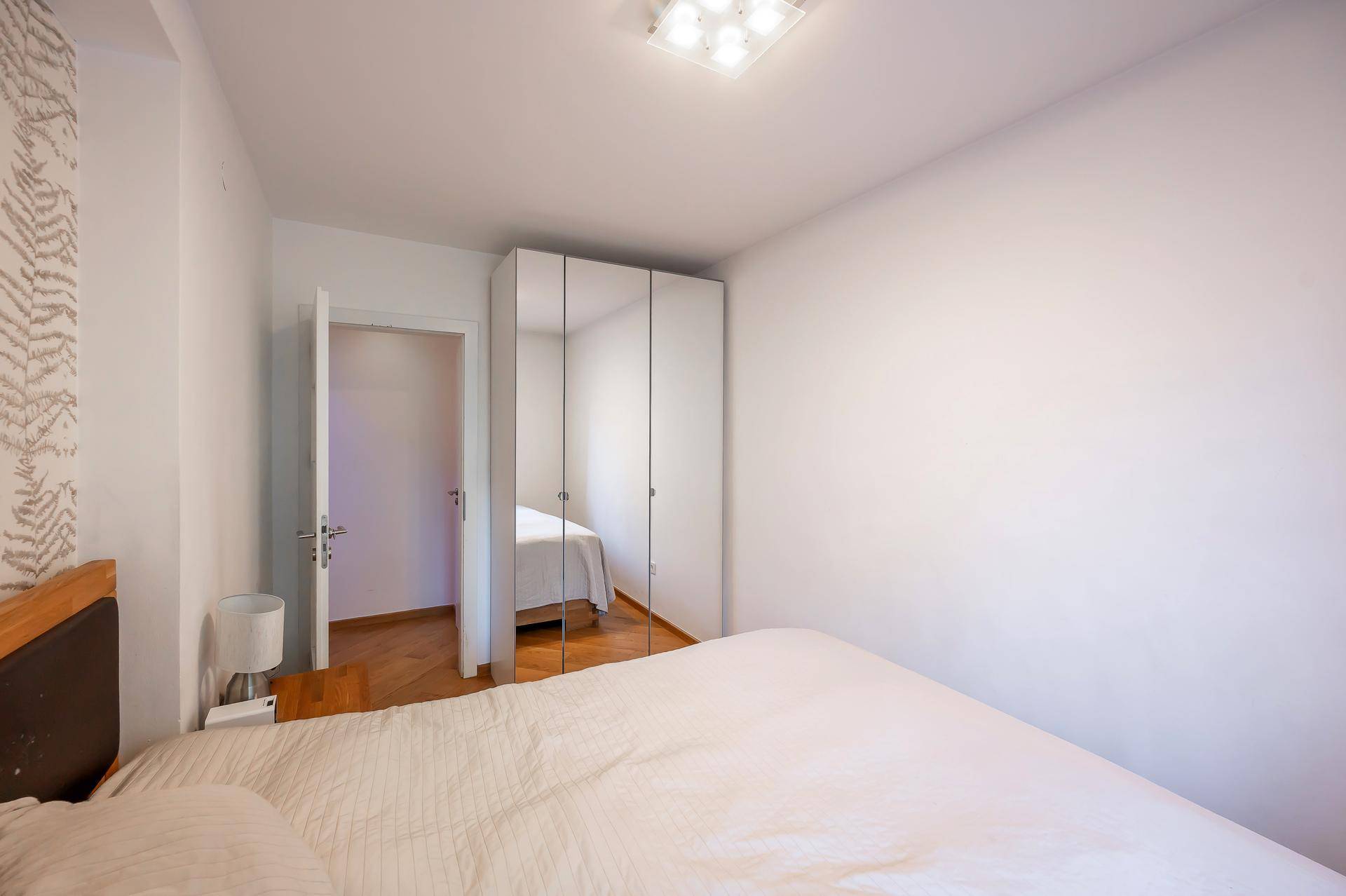 Helles Schlafzimmer mit Holzboden, weißem Kleiderschrank und minimalistischer Einrichtung.
