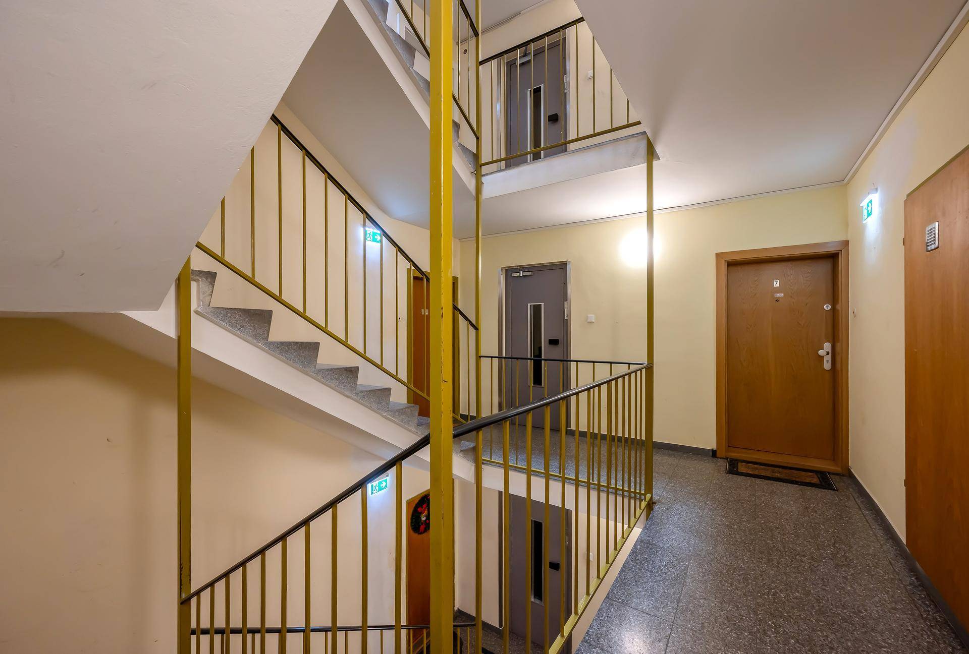 Treppenhaus eines Mehrfamilienhauses mit gefliestem Boden und gelbem Metallgeländer.