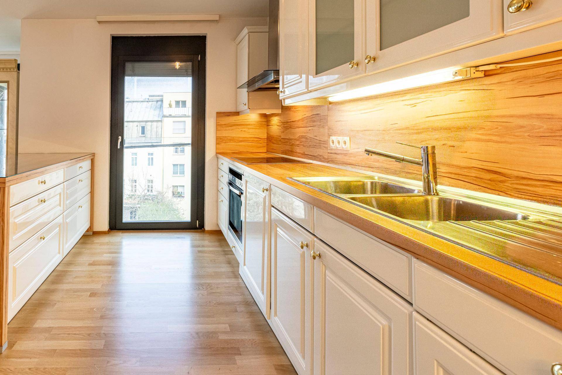 Helle Küche mit weißen Schränken, Holzoptik-Arbeitsplatten und Zugang zu einem Balkon.