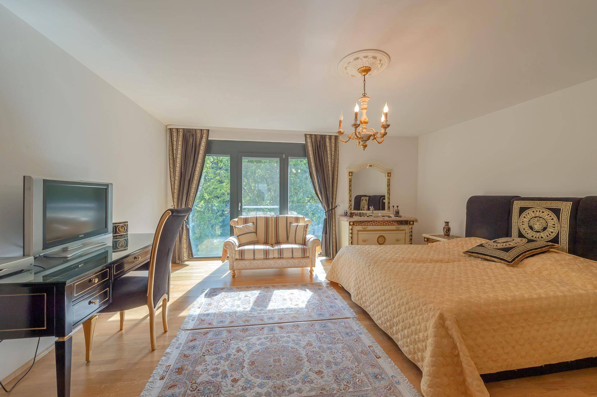 Helles Schlafzimmer mit Doppelbett, Schreibtisch und Zugang zu einem Balkon mit Blick ins Grüne.