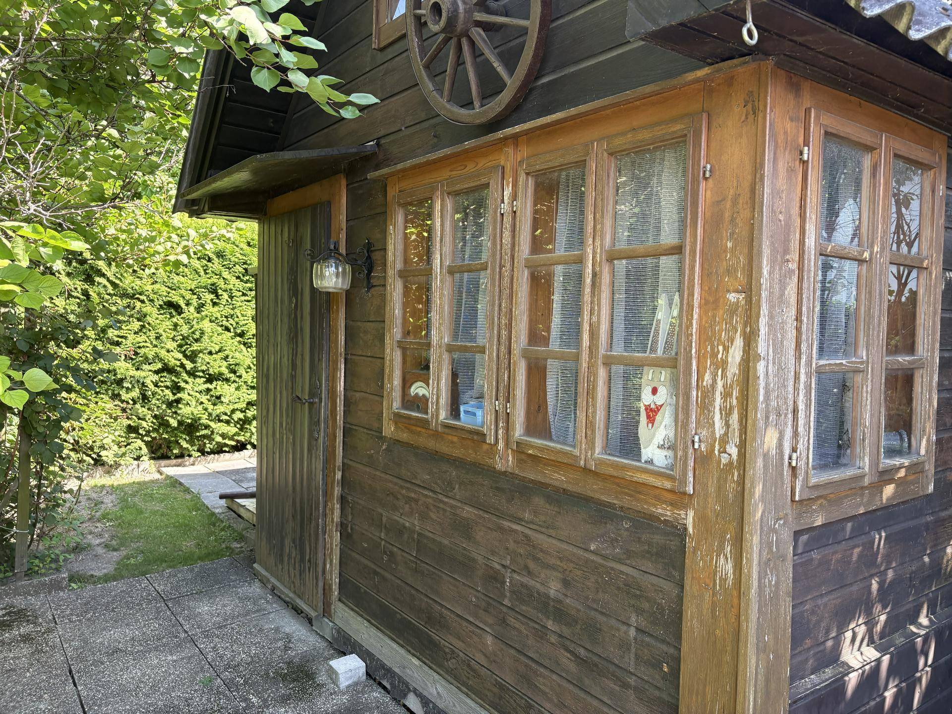 Kleines Holzgebäude mit mehreren Fenstern und rustikalem Wagenrad als Dekoration.