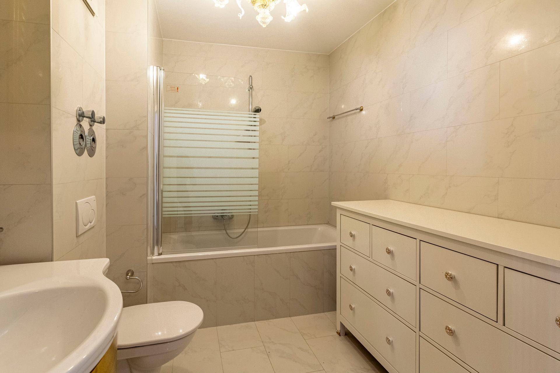Helles Badezimmer mit Badewanne, Duschabtrennung und weißem Waschtischunterschrank.