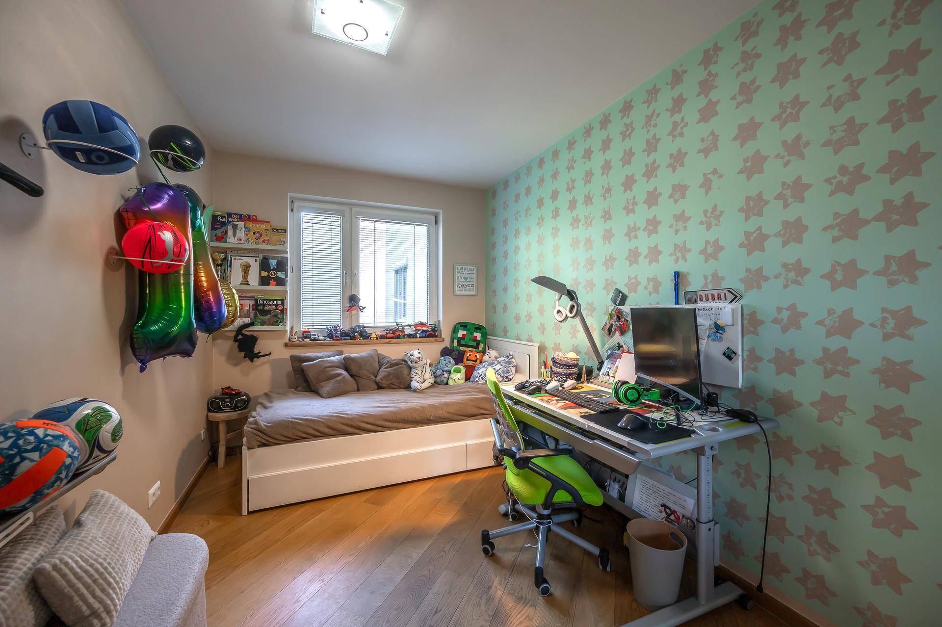Kinderzimmer mit Holzboden, Schreibtisch, Bett und bunter Sternen-Tapete.