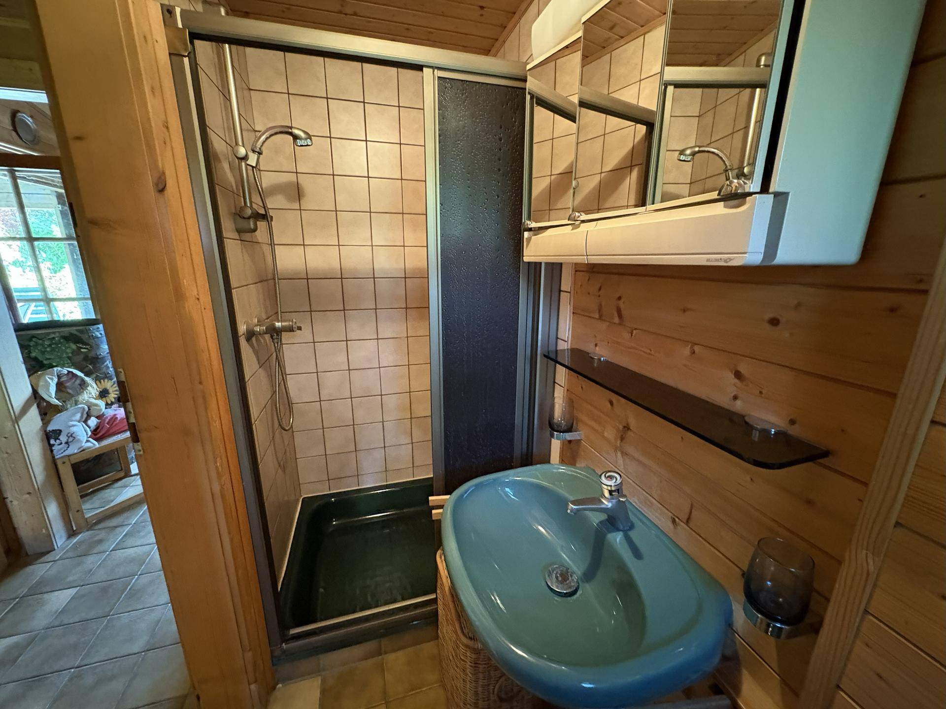 Kleines Badezimmer mit Duschkabine, blauem Waschbecken und Holzwänden im Landhausstil.
