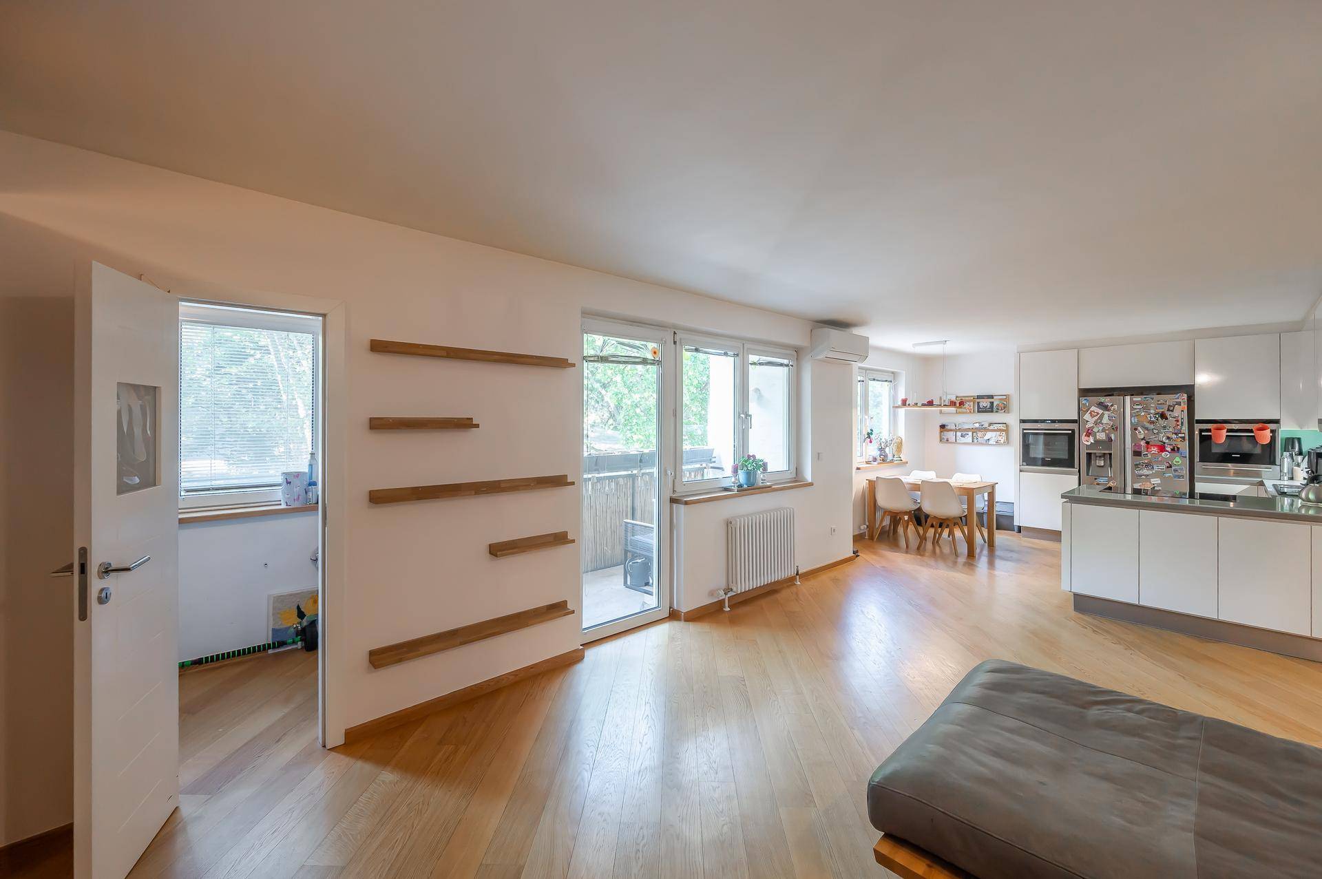 Heller Wohn-Essbereich mit offener Küche, Holzboden und Zugang zum Balkon.