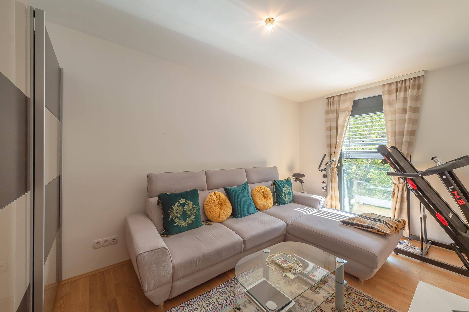 Gemütliches Zimmer mit Sofa, Couchtisch und Trainingsgeräten, mit Zugang zum Balkon.