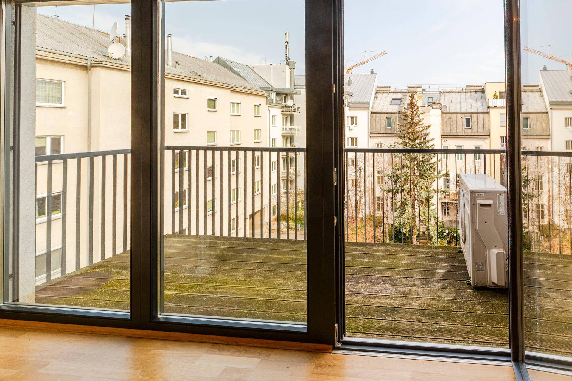 Blick vom Innenraum auf einen Balkon mit Holzboden und Stadtansicht.