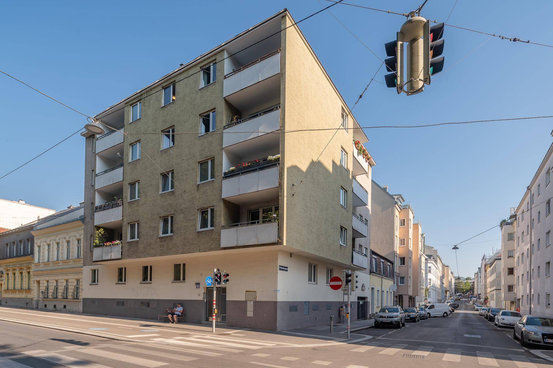 Mehrfamilienhaus an einer Straßenecke mit Balkonen und umliegender Stadtbebauung.