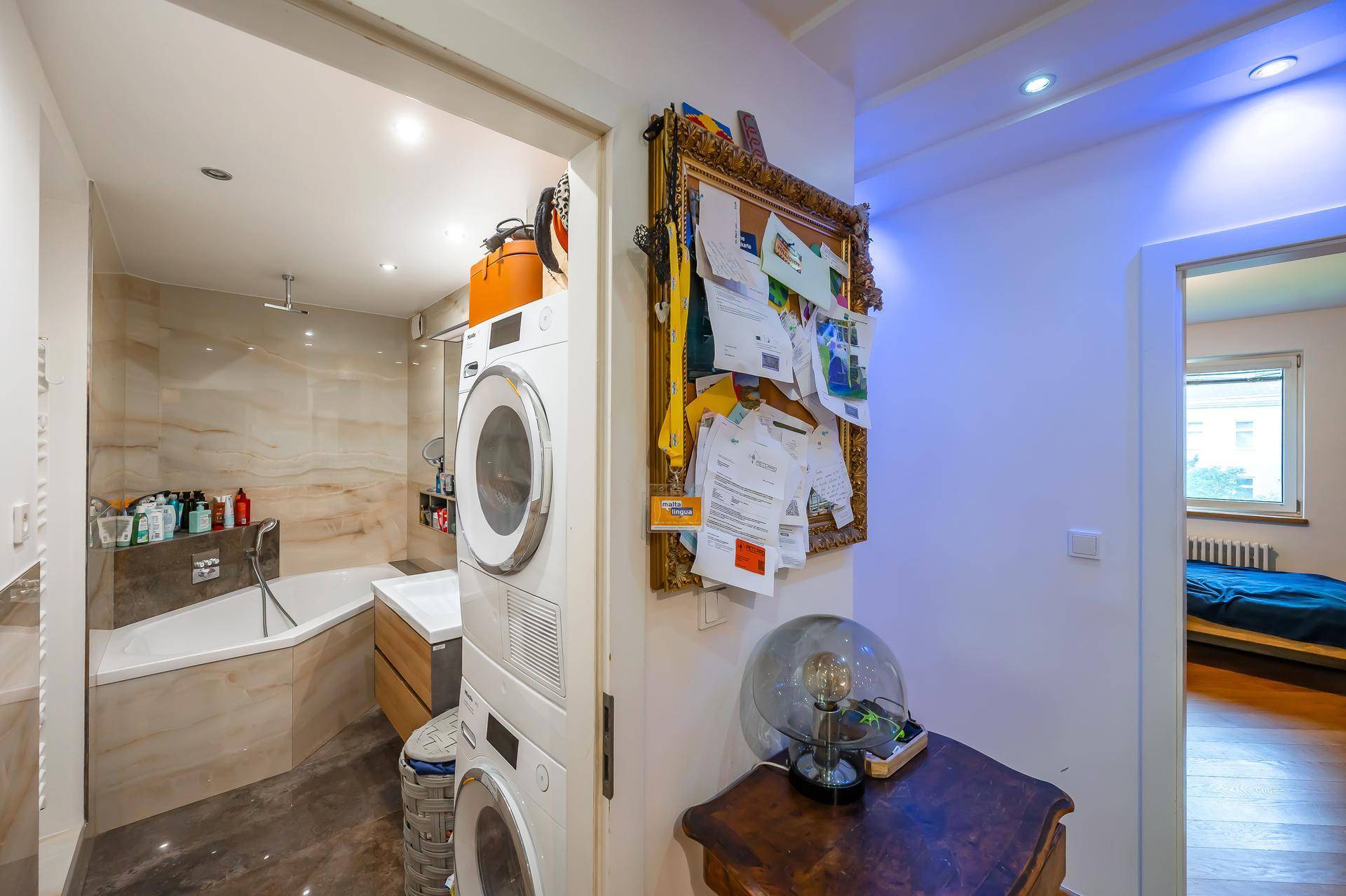 Badezimmer mit Eckbadewanne, Waschmaschine und Trockner, gefliest in Natursteinoptik.