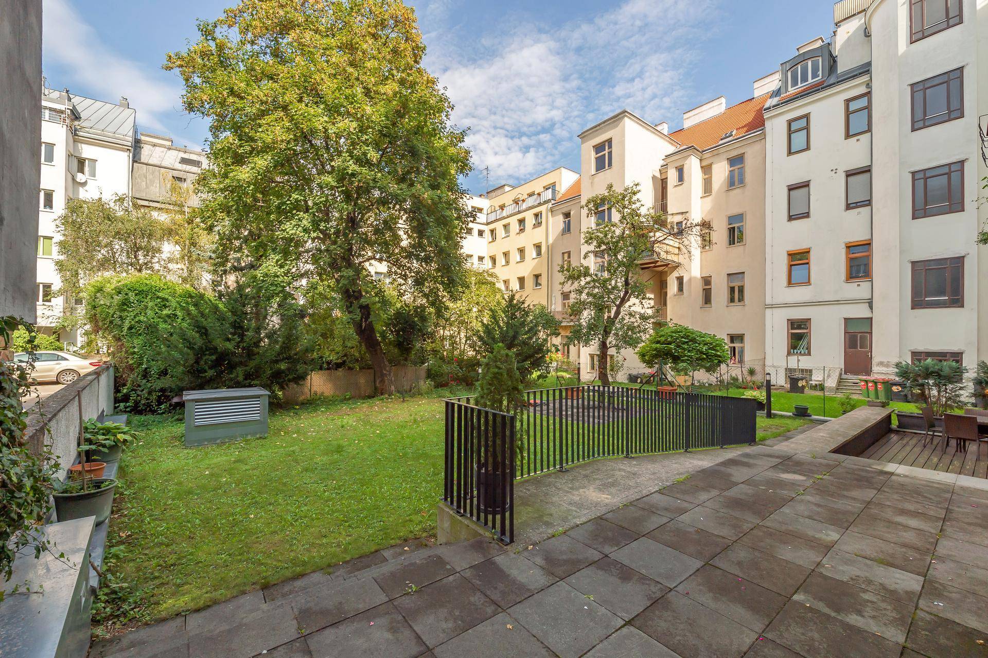 Gepflegter Gemeinschaftsgarten mit Rasenfläche, Bäumen und Sitzgelegenheiten zwischen Gebäuden.