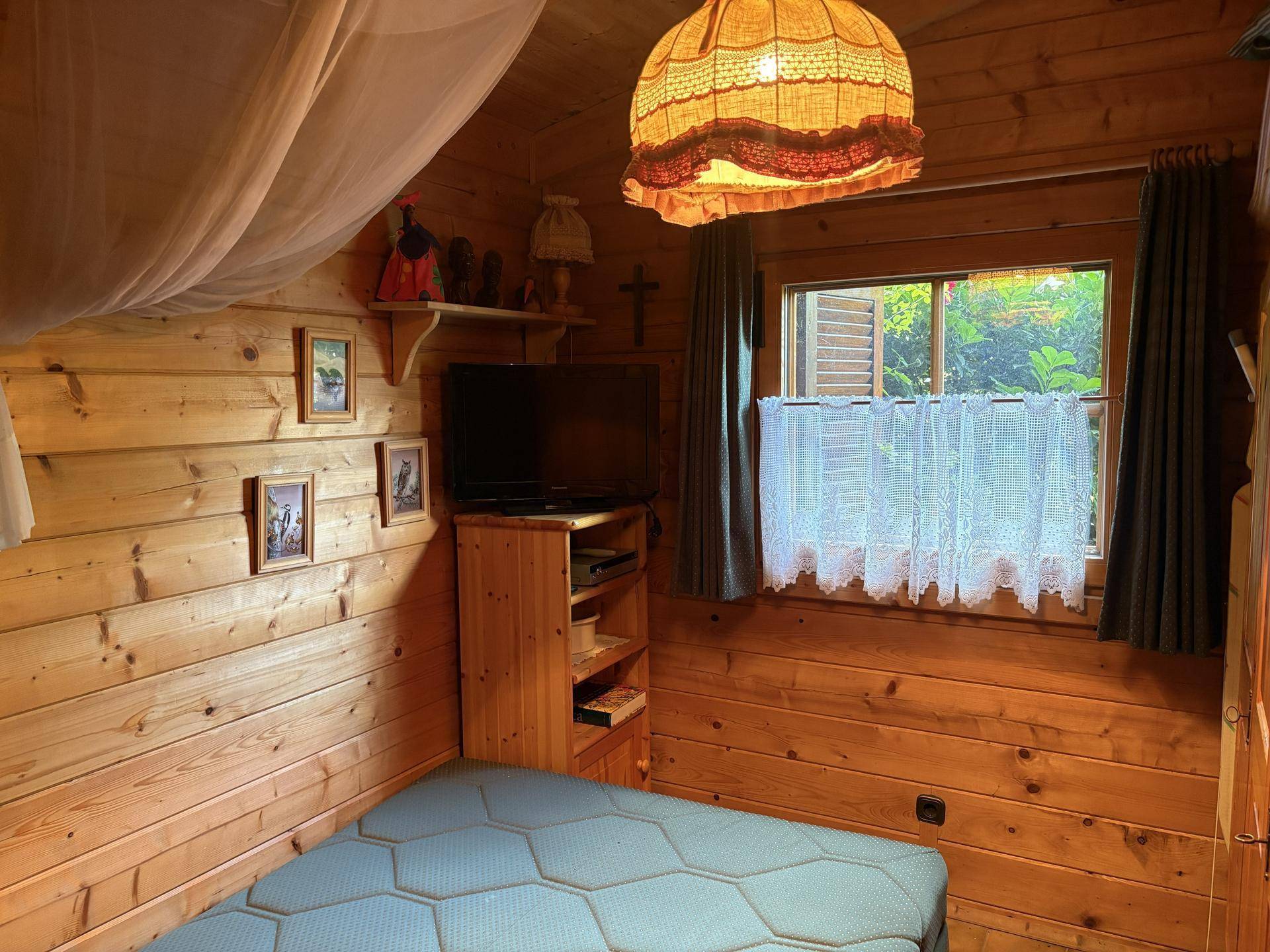 Kleines Schlafzimmer mit Holzwänden, einem Einzelbett und einem Fenster mit Vorhängen.