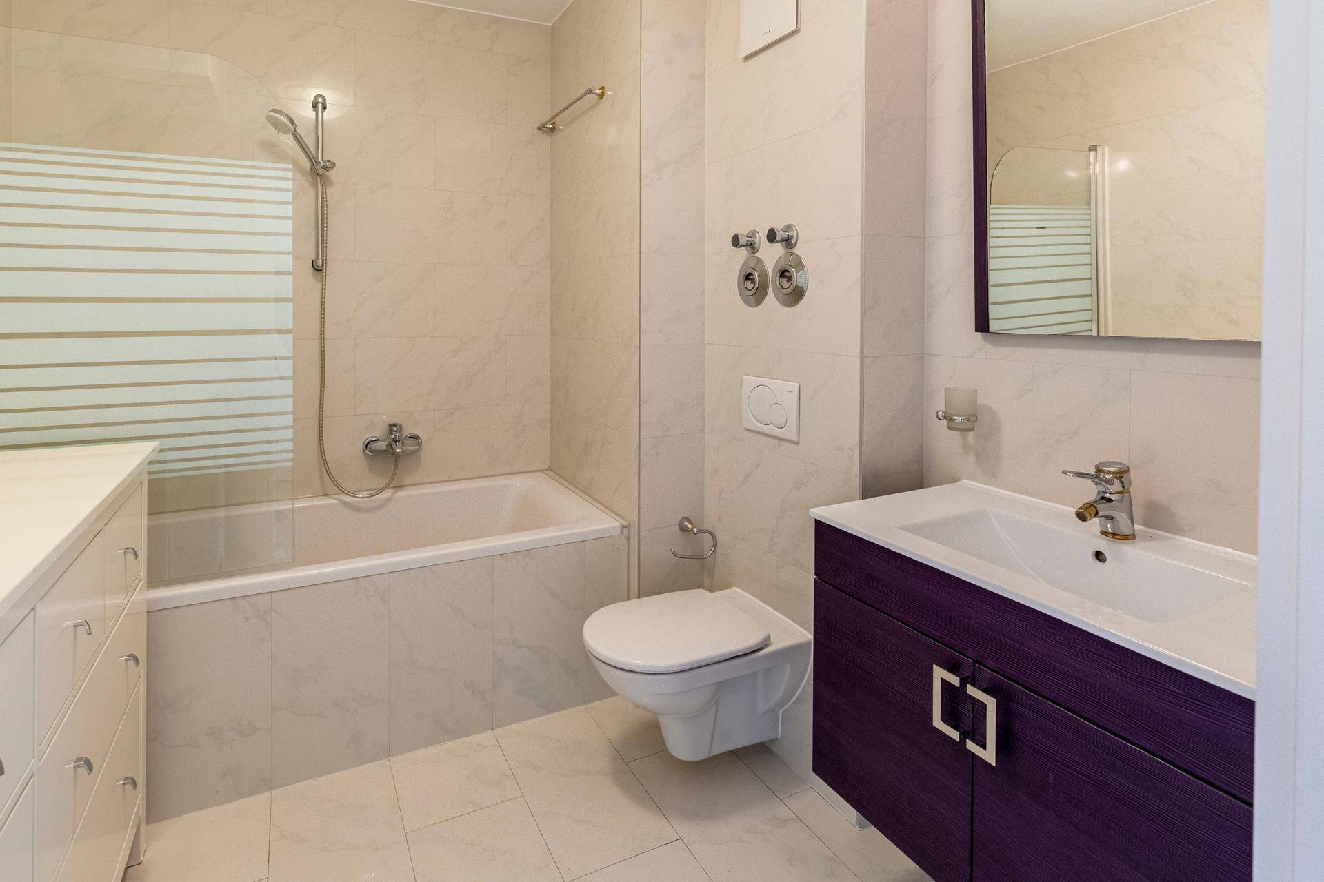 Modernes Badezimmer mit Badewanne, Duschabtrennung und lila Waschtischunterschrank.