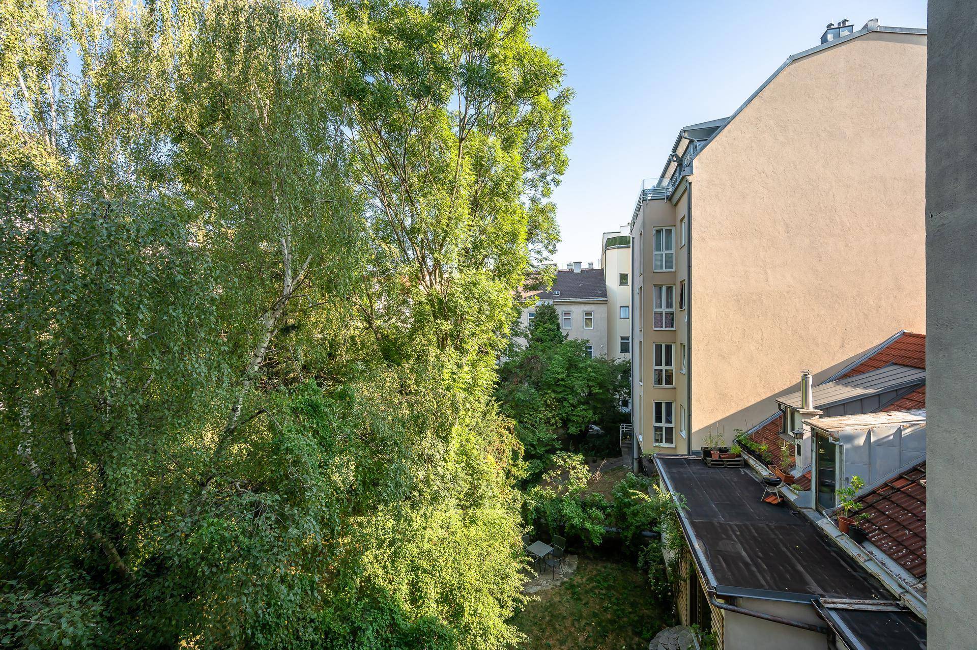 Blick von oben auf einen grünen Hinterhofgarten mit Bäumen und angrenzenden Gebäuden.