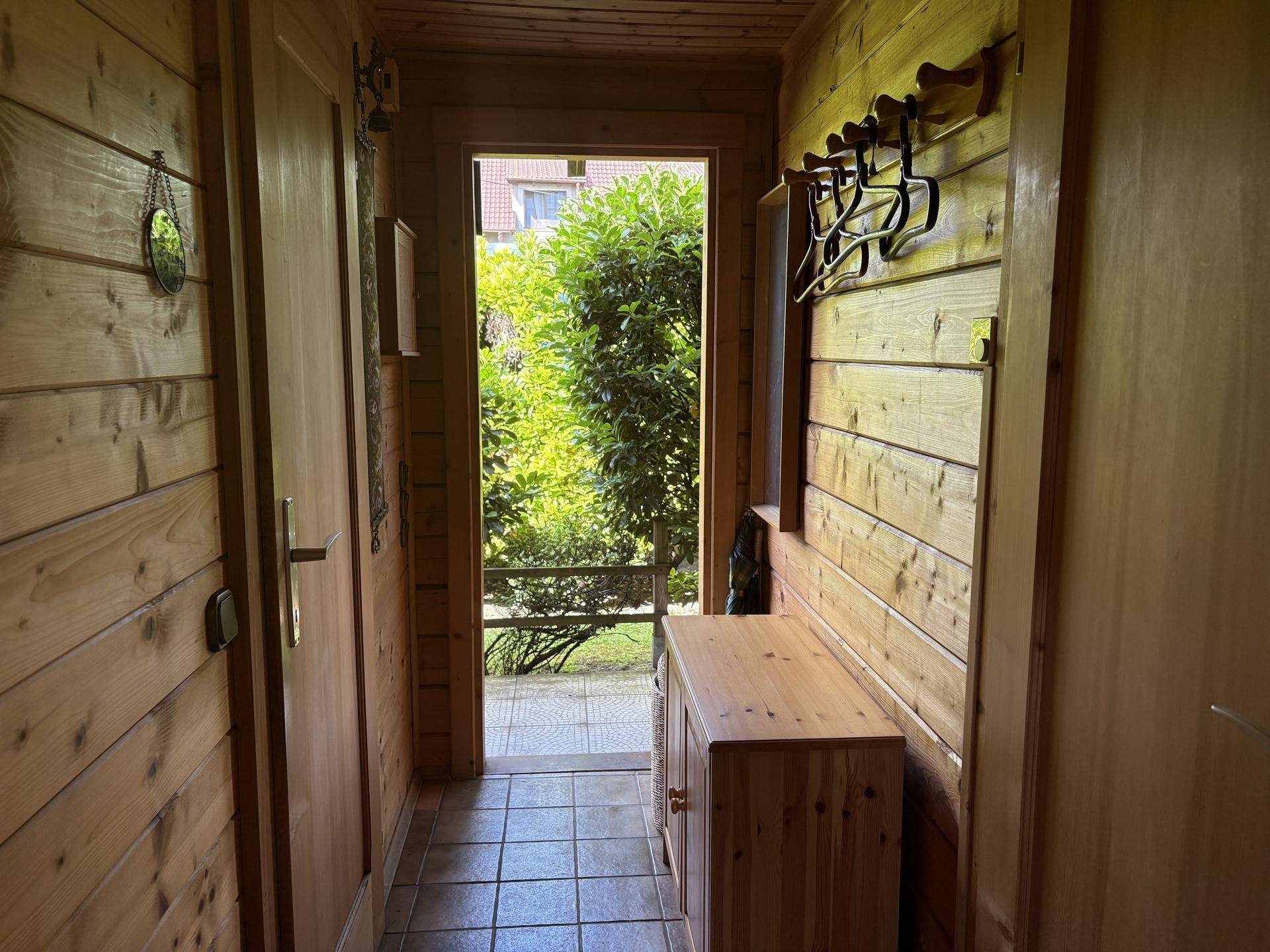 Schmaler Flur mit Holzwänden, Garderobe und Blick nach draußen durch die Eingangstür.