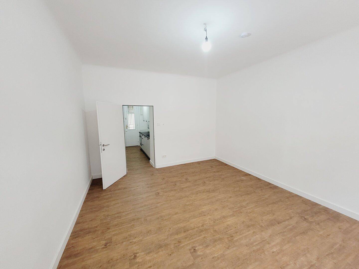 Heller Wohnraum mit Holzboden und Zugang zu einer modernen Küche, ideal für offenes Wohnen.
